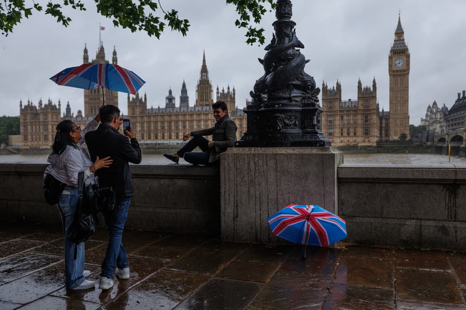 LONDON, UNITED KINGDOM - JUNE 03: Tourists take photographs opposite the Houses of Parliament in heavy rain on June 03, 2026 in London, United Kingdom. The Met Office has issued a weather warning that heavy rain and thunderstorms are expected across the whole country. (Photo by Dan Kitwood/Getty Images)