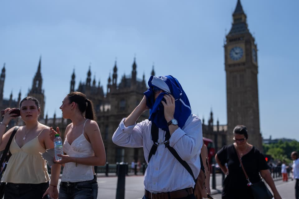<p>A man holds a t-shirt over his head to shelter from the sun as he walks through central London on June 24</p>