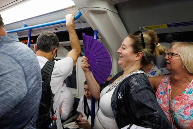 <p>A passenger uses a handheld fan on the Tube as temperatures rise</p>