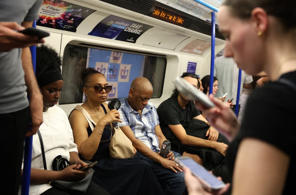 <p>A person uses a portable fan on an underground train in central London on June 24</p>
