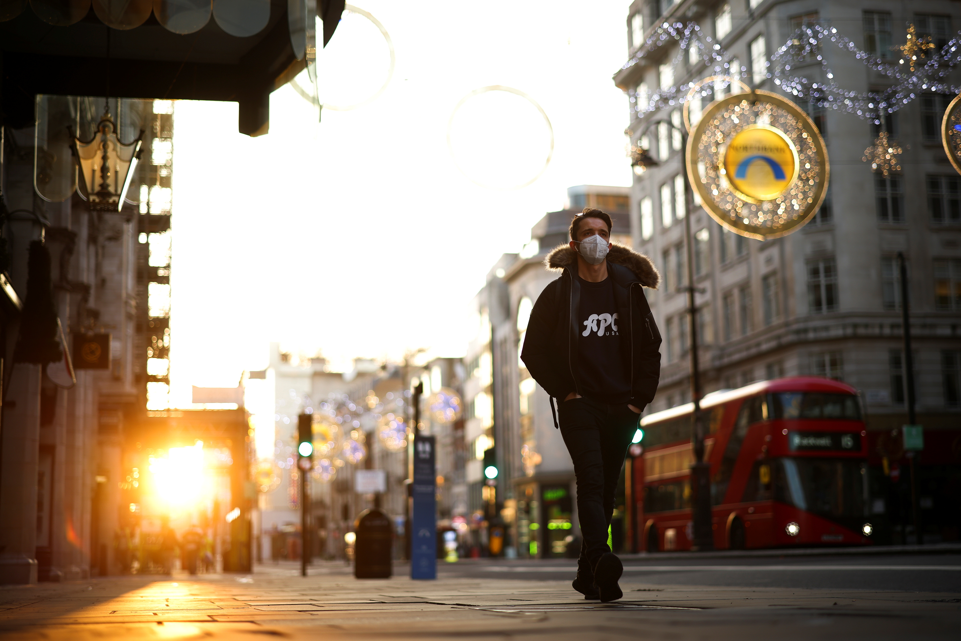 A man wearing a protective face mask walks down Strand during sunset, amid the coronavirus disease (COVID-19) outbreak, in London