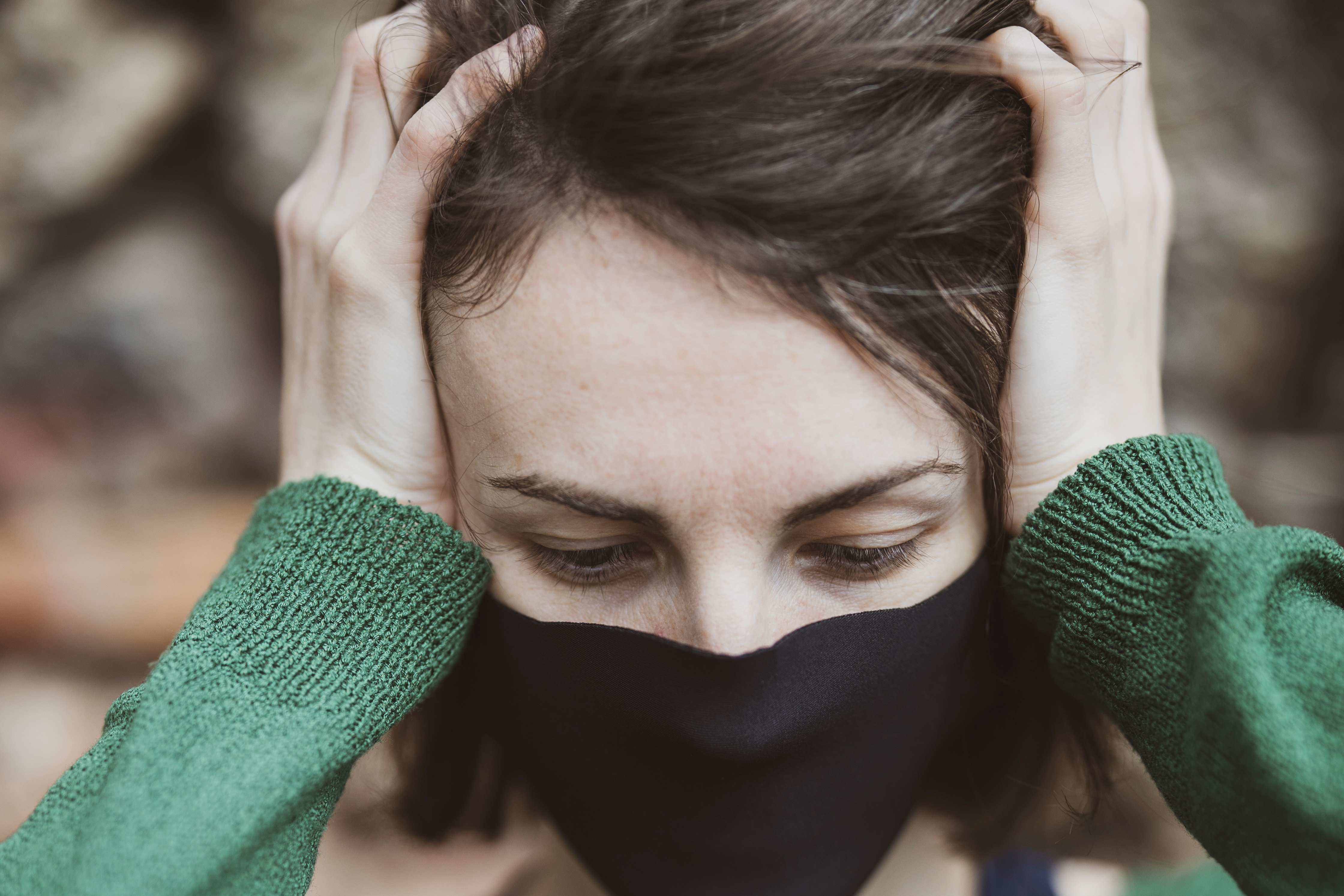 Woman wearing face mask holds head