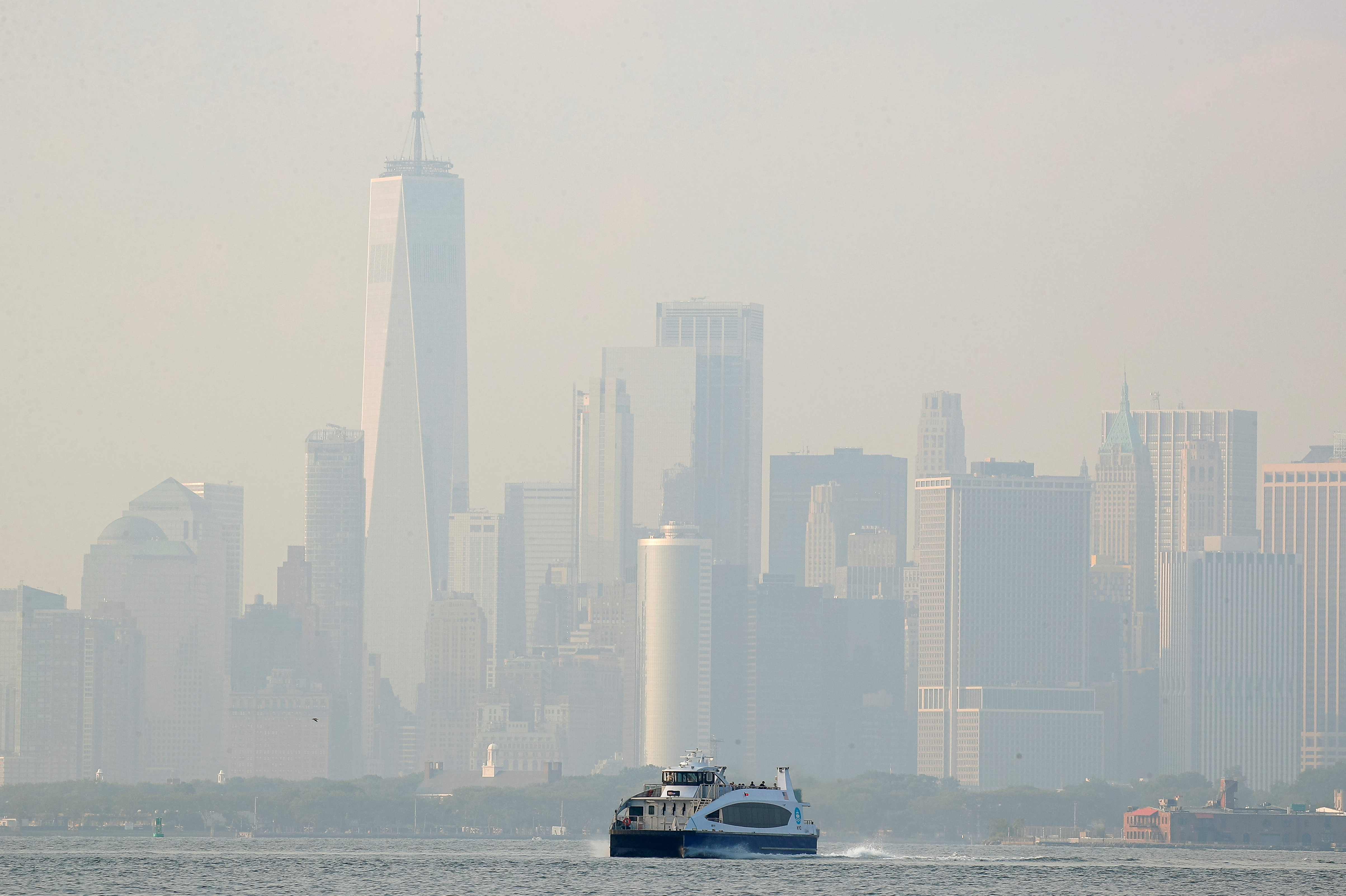 The lower Manhattan skyline is seen through a cover of wildfire smoke as a NYC Ferry makes its way through the Upper Bay as seen from Brooklyn, New York