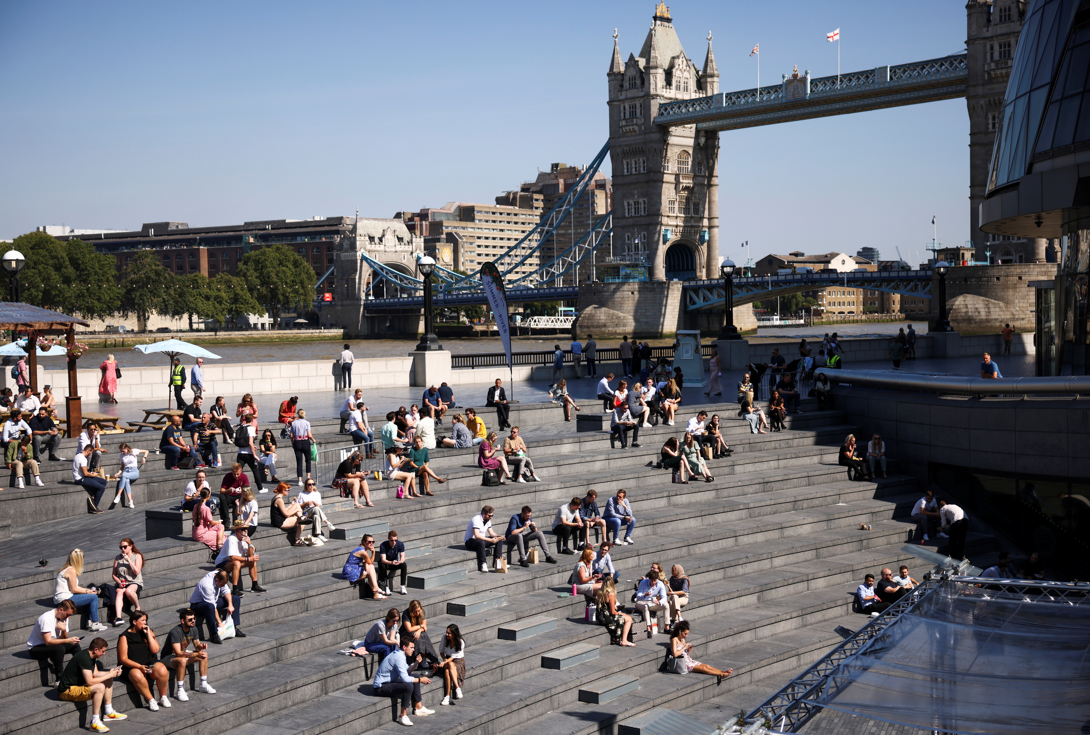 Tower Bridge can be seen in the background as people relax in the sunny weather