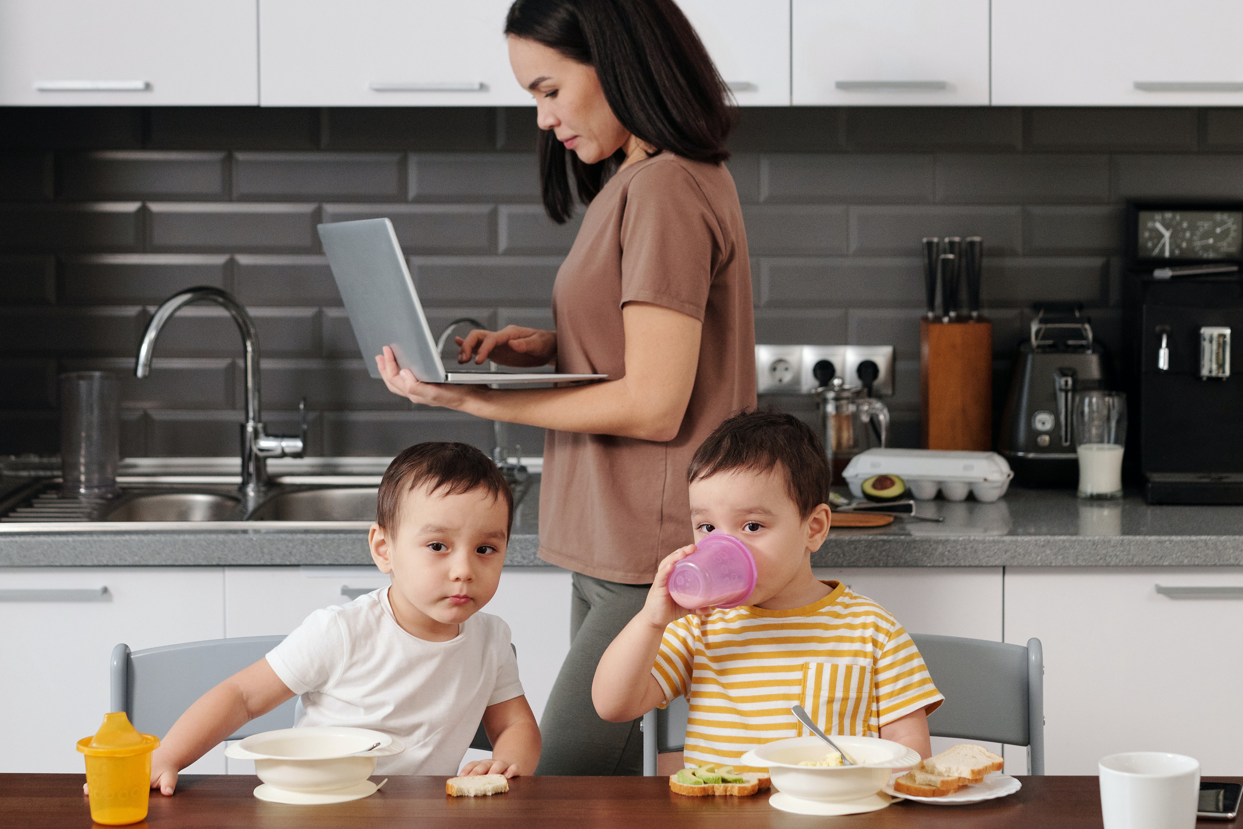 Children eating breakfast at the table as the mother works on her laptop