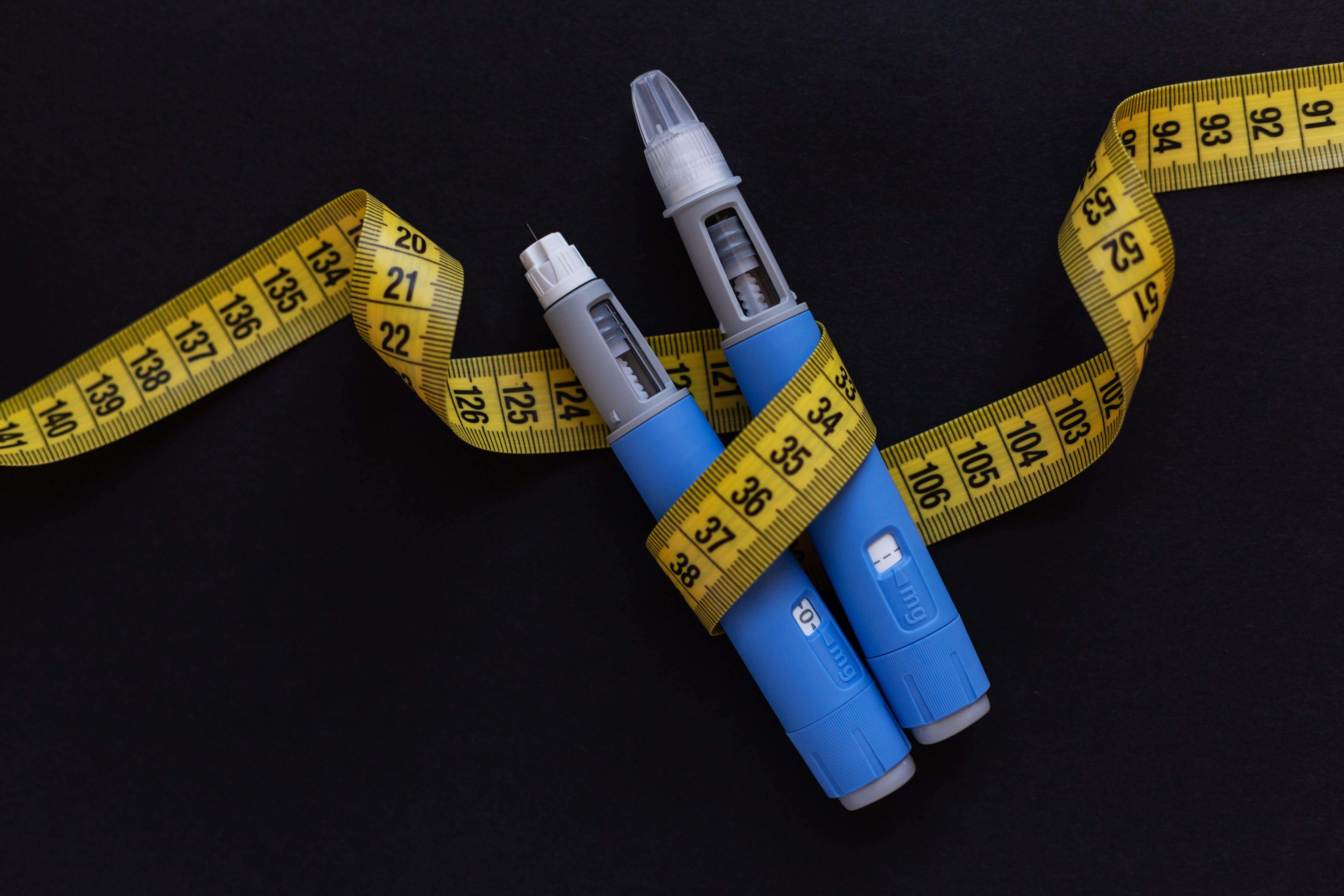Ozempic pens wrapped around in body measurement tape