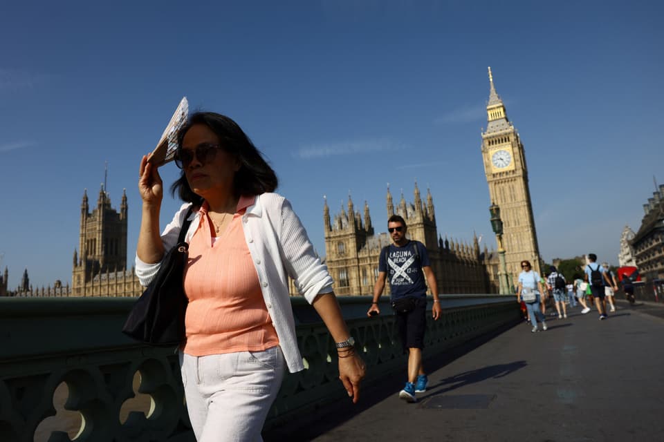 A woman shields her face from the sun as she croses Westminster Bridge during a heatwave,